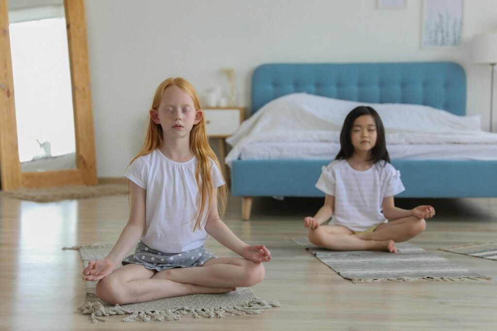 Mindfulness and Child Development: Growing Calm, Focused, and Emotionally Resilient Minds Full body of concentrated diverse girls meditating on carpets in bright cozy room next to mirror and big bad in daylight
