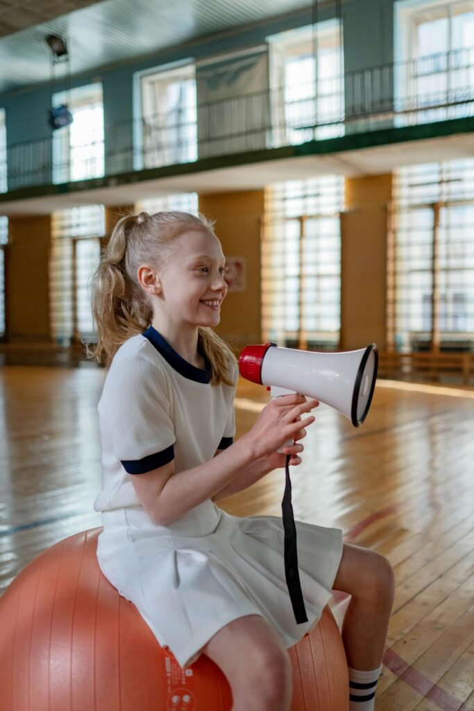 November’s World Communication Week: How Bilingual Families Can Turn Every Conversation into a Mindful, Emotionally-Intelligent Moment Young girl with a megaphone sitting on a fitness ball indoors, smiling and relaxed.